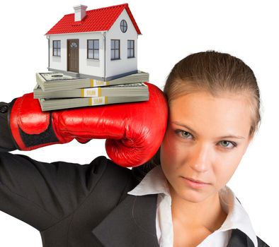 Businesswoman in boxing gloves with bundle of money and house looking at camera on isolated white background