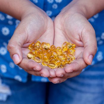 Pills of fish oil holding by young girl.