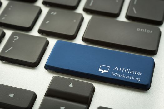 Close up laptop keyboard focus on a blue button with typographic word AFFILIATE MARKETING and computer sign. Internet and business concepts.