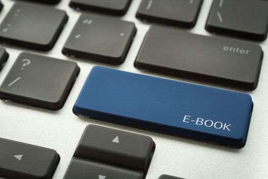 Close up laptop keyboard focus on a blue button with typographic word E-BOOK. Internet technology and education concepts.