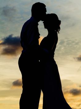 Silhouettes of bride and groom kissing at  sunset.