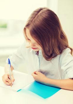 education and school concept - little student girl writing in notebook at school