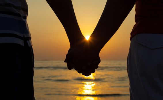 Silhouettes couples holding hands on sunset.