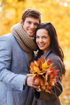 love, relationship, family and people concept - smiling couple with bunch of leaves hugging in autumn park