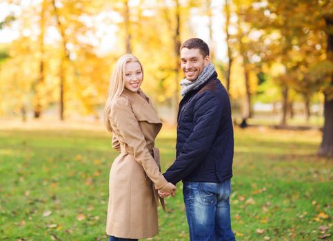 love, relationship, family and people concept - smiling couple holding hands in autumn park