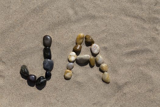 A set of pebbles in a sandy beach forming the swedish word for Yes