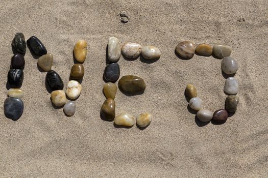 A set of pebbles in a sandy beach forming the swedish word for No.
