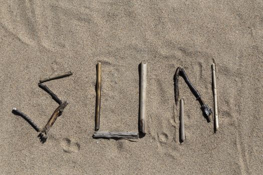 A set of sticks in a sandy beach forming the word sun