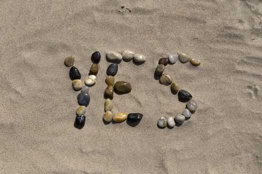 A set of pebbles in a sandy beach forming the word yes