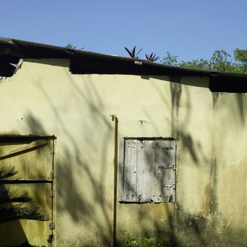 Rundown front door and closed window shutter of a yellow house in the tropics