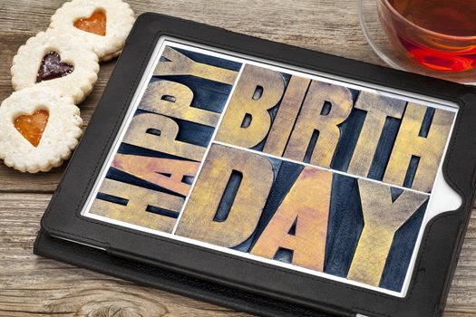 happy birthday typography - isolated text abstract in letterpress wood type printing blocks on a digital tablet with tea and heart cookies