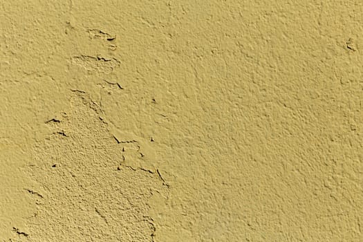 A grained yellow concrete wall with texture, some of the parts are falling of