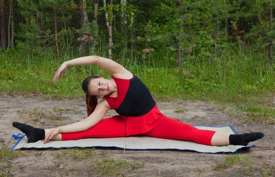 Pretty woman doing yoga exercises in the woods sitting on the splits