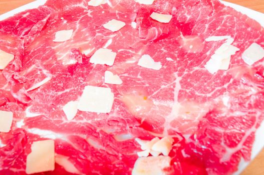 White dish with carpaccio of beef with parmesan.