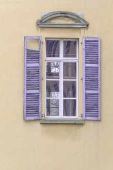 Old window with purple wooden shutters on a beige facade.