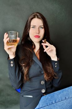 Pretty brunette model holding glass of whisky and cigar. Girl with confident face expression, wearing dark tail-coat.