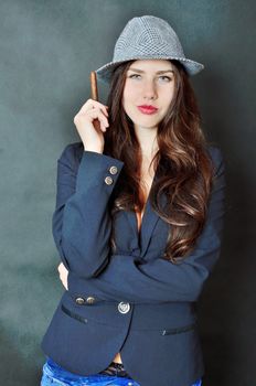 Girl with tail-coat and hat. Female model holding cigar, confident brunette.