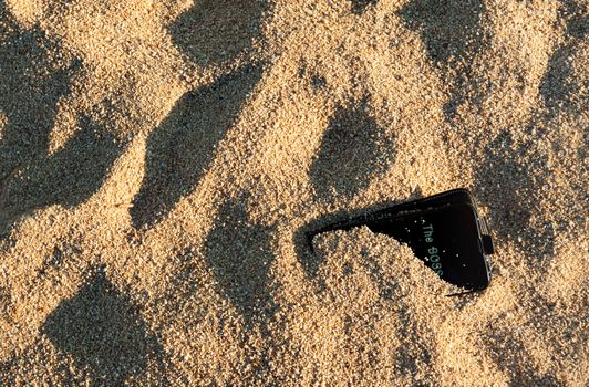 A black smart phone left buried in the send on a beach with the boss calling.