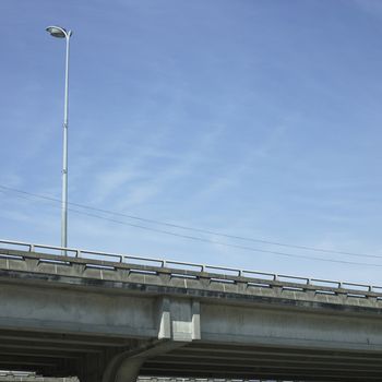 Concrete highway overpass with tall streetlight and blue sky