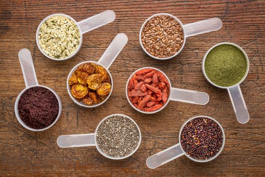 superfood abstract (wheatgrass, acai berry, goji berry, falx seed,chia seed,goldenberry,hemp seed, quinoa grain) - top view of measuring scoop against rusti wood