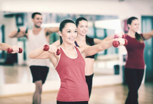 fitness, sport, training, gym and lifestyle concept - group of smiling people working out with dumbbells in the gym