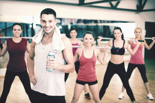 fitness, sport, training, gym and lifestyle concept - smiling trainer in front of group of people working out with barbells in the gym