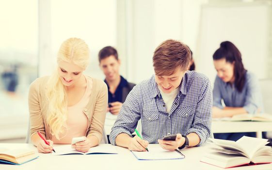 education and technology concept - group of students looking into smartphone at school