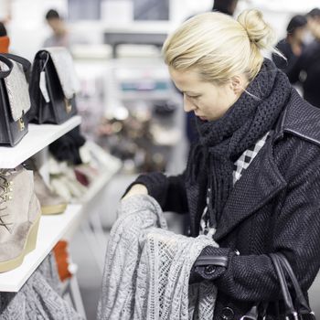 Woman shopping clothes. Shopper looking at clothing indoors in store. Beautiful blonde caucasian female model. 