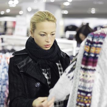 Woman shopping clothes. Shopper looking at clothing indoors in store. Beautiful blonde caucasian female model. 