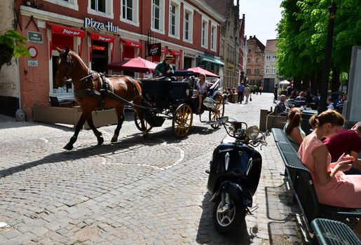 Bruges, Belgium - May 11, 2015: Tourists visit Bruges in traditional horse carriage around the city. Bruges is the capital and largest city of the province of West Flanders in the Flemish Region of Belgium.