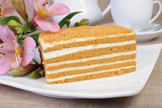Piece of honey cake with a cup of coffee on a table with a flower