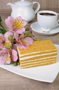 Piece of honey cake with a cup of coffee on a table with a flower