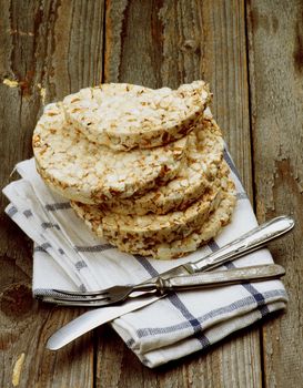 Health Eating Concept with Stack of Puffed Spelt Oat Galettes, Silverware Fork and Knife on Checkered Napkin closeup on Rustic Wooden background