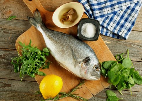 Cooking Raw Dorado Fish with Arugula, Herbs, Spices, Anchovies and Lemon on Wooden Cutting Board closeup. Top View