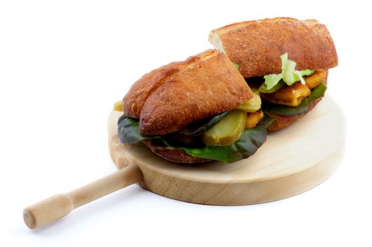 Delicious Fish Burgers with White Fish Sticks, Lettuce, Gherkins and Whole Wheat Bread on Circle Wooden Cutting Board isolated on white background