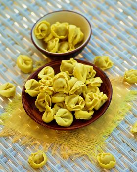 Raw Meat Cappelletti in Brown Bowls with Yellow Napkin closeup on Wicker background. Selective Focus