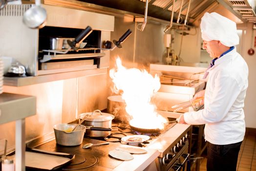 Male chef cooking in a frying pan on a kitchen 