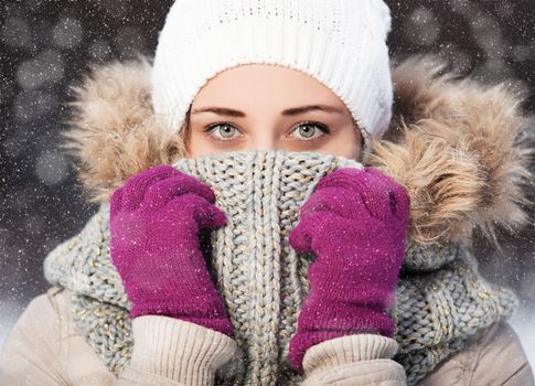 Portrait of a beautiful girl in a scarf and gloves in winter park. flying snow