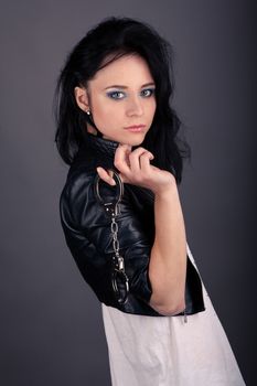 pretty girl in leather jacket with police handcuffs on a gray background