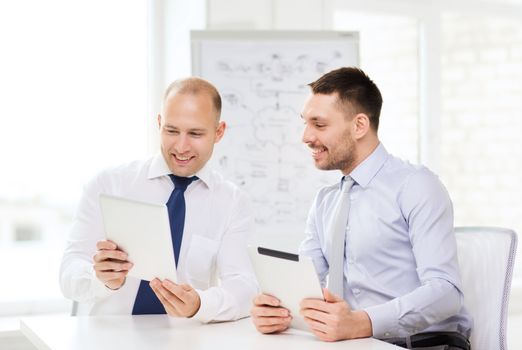 business, technology and office concept - two smiling businessmen with tablet pc computers in office