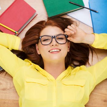 education and home concept - smiling redhead female student in eyeglasses lying on floor