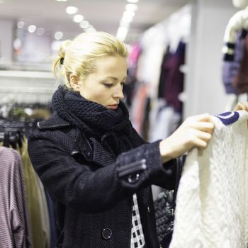 Woman shopping clothes. Shopper looking at clothing indoors in store. Beautiful blonde caucasian female model. 