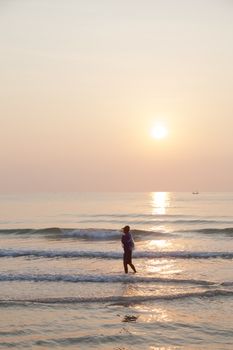 Man walking on the beach. In the morning the sun rises over the ocean.