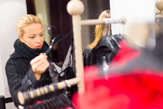 Woman shopping clothes. Shopper looking at clothing indoors in store. Beautiful blonde caucasian female model wearing casual winter clothing and black scarf.