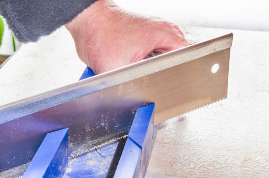 Hand of a worker with miter saw against a bright background.