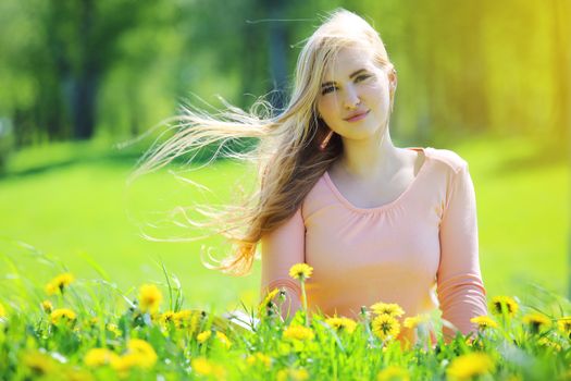 Beautiful young woman laying in spring park with dandelion flowers