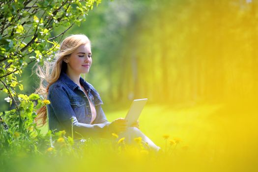 Young woman using tablet in spring park with flowers