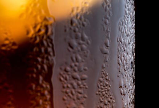 A macro shot of condensation forming and dripping down a glass of tea with ice in it on a black background.