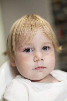 portrait of blonde caucasian baby nineteen month age chubby face looking at camera with serious expression