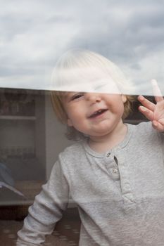 portrait of smiling blonde caucasian baby nineteen month age chubby face looking at camera through reflecting glass door